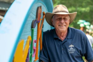 Kids Kingdom curator, Henry stands next to the entrance sign to the Kids Kingdom area of the zoo. He wears a navy blue staff shirt and a cowboy hat.