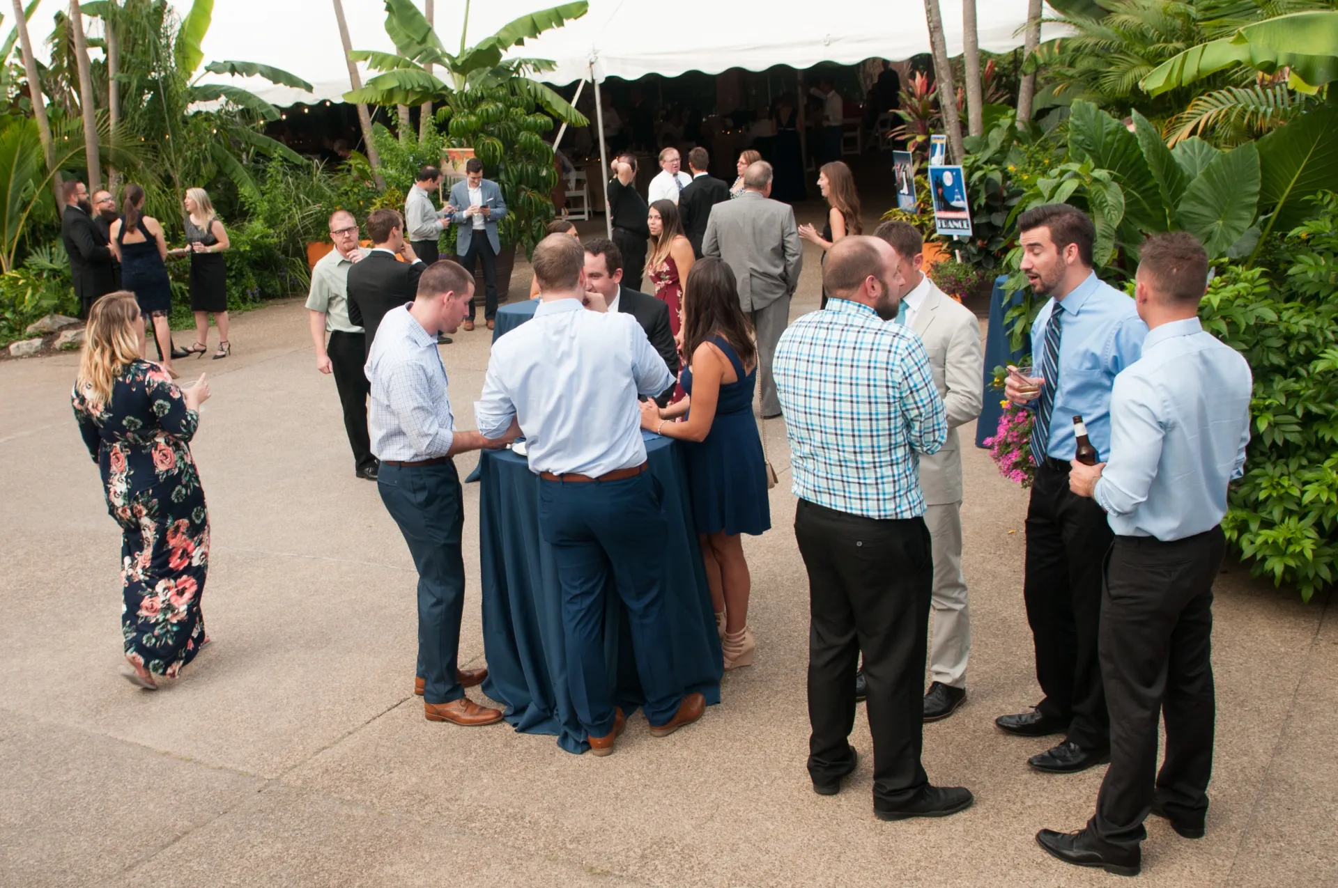 a group of guests in cocktail dress outside the garden tent. they are talking and enjoying beverages.