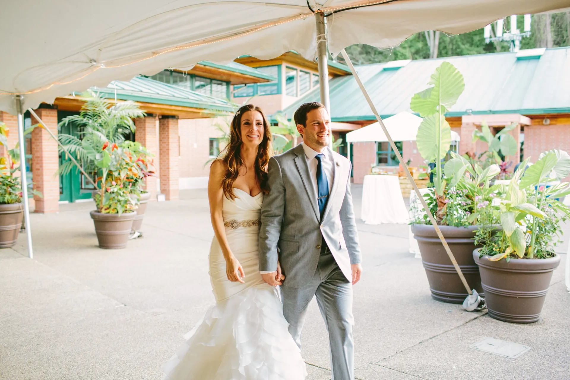 a bride and groom holding hands and walking into the garden tent